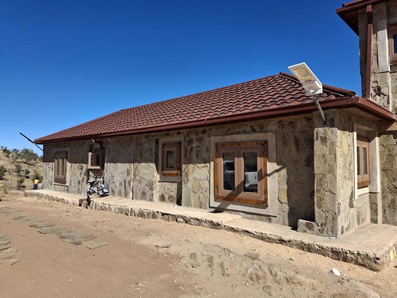 Exterior view of a stone-clad building featuring a tiled roof, wooden window frames, and an installed solar security light on a rural small holding.
