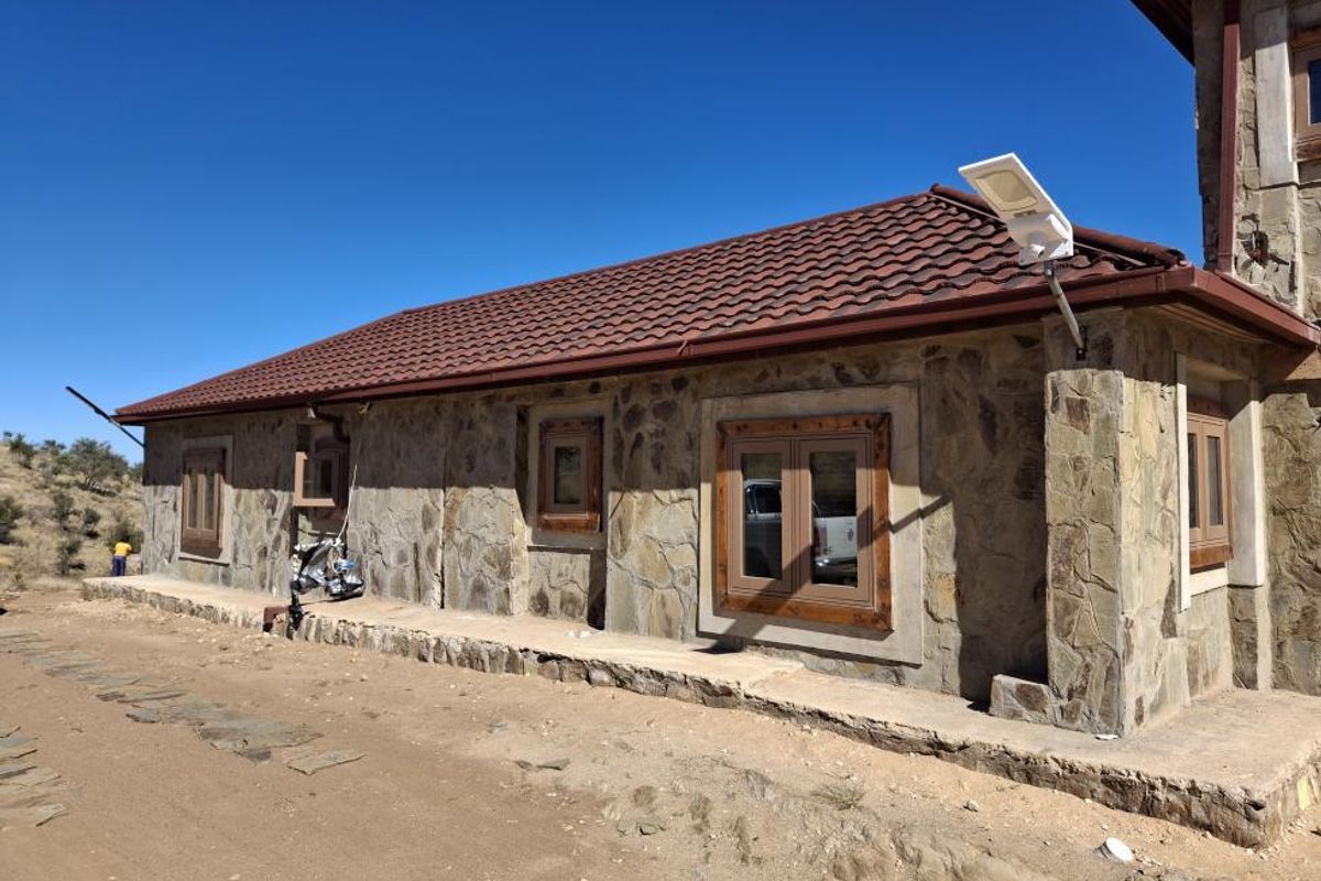 Exterior view of a stone-clad building featuring a tiled roof, wooden window frames, and an installed solar security light on a rural small holding.