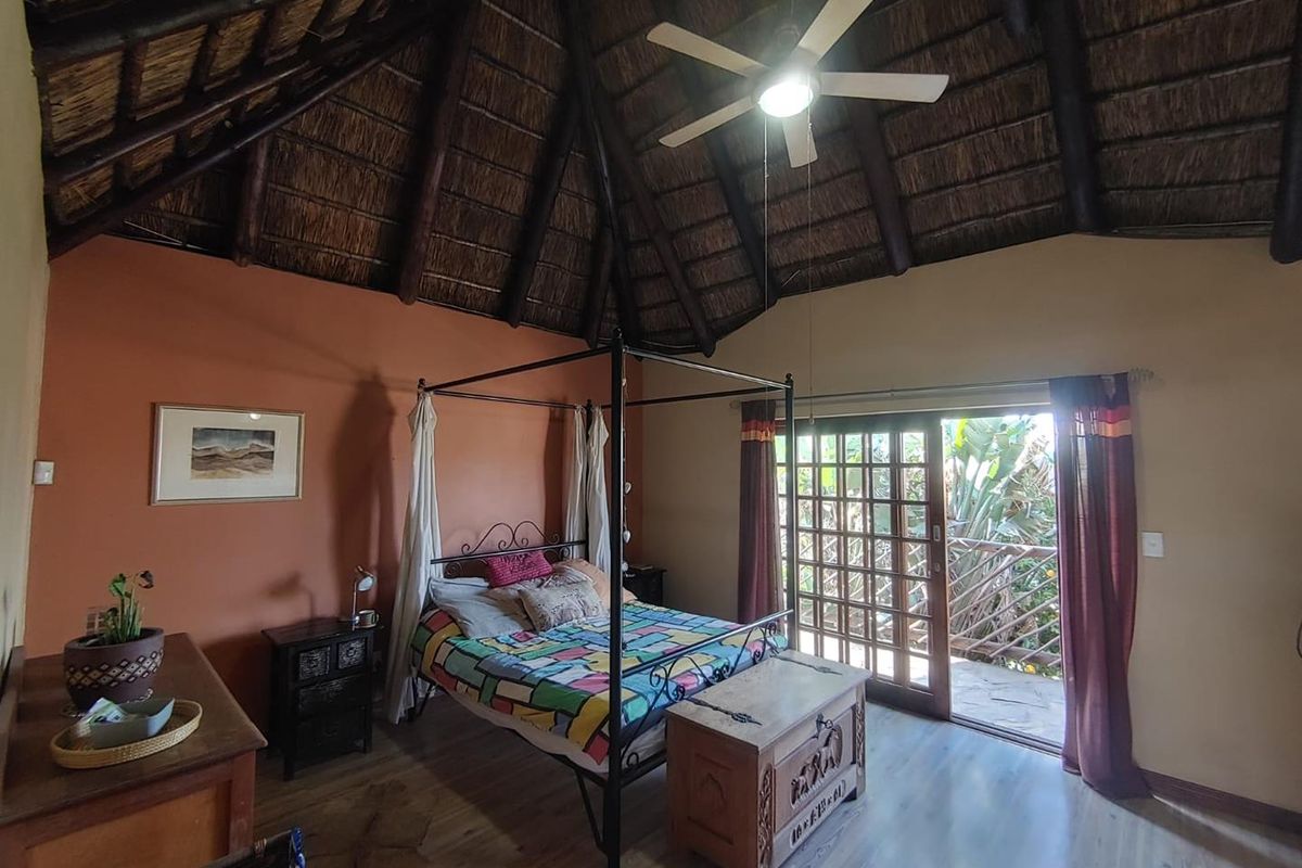 Spacious bedroom featuring a high vaulted thatched ceiling, exposed timber beams, ceiling fan, and sliding glass doors opening onto a private balcony.