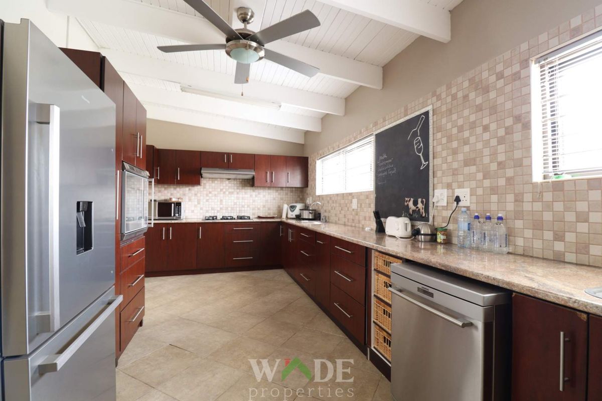 Spacious kitchen featuring dark wood cabinetry, granite countertops, tiled backsplash, and a vaulted ceiling with a central fan.