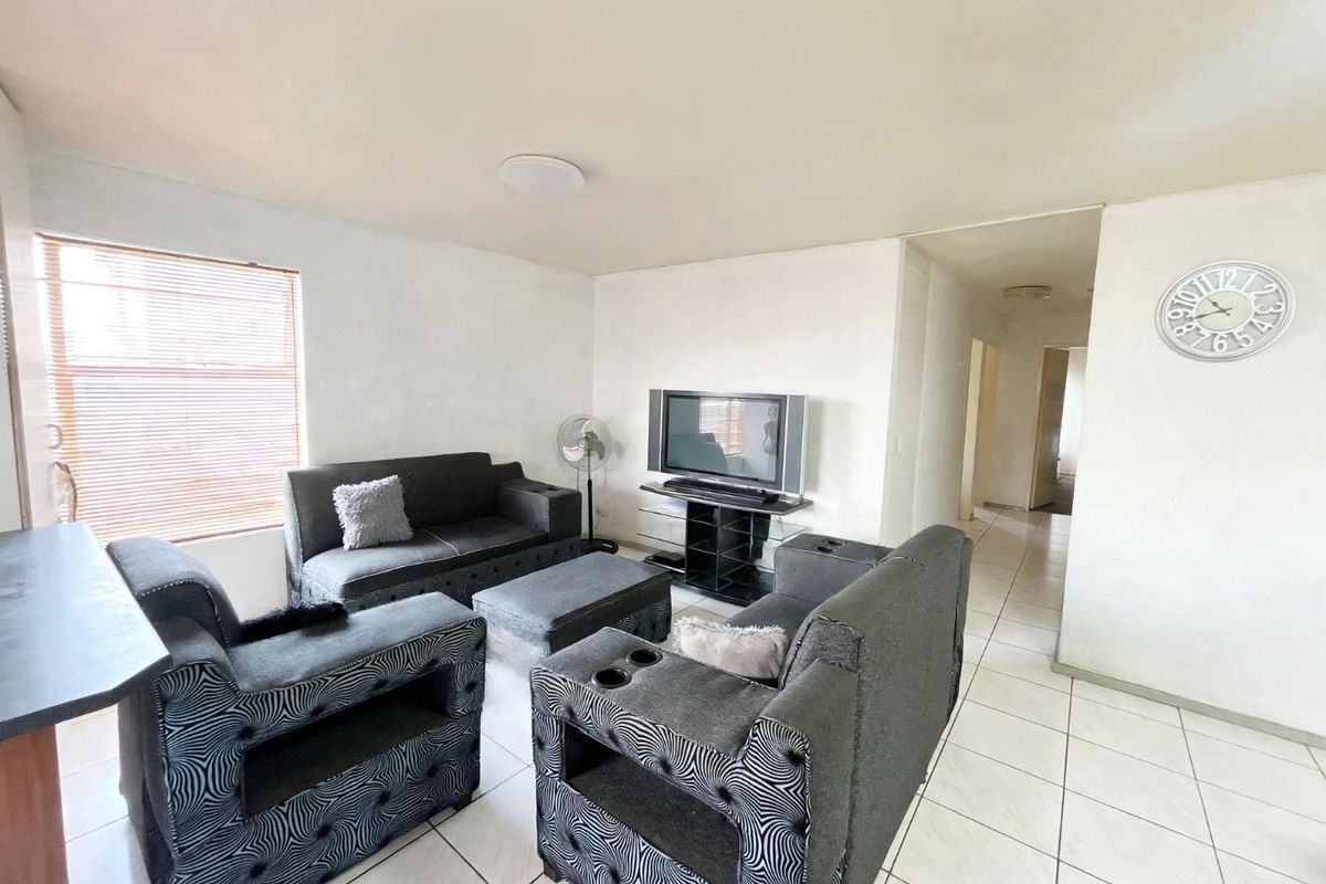 A living room area featuring tiled flooring, neutral walls, and venetian blinds, providing a functional space with potential for cosmetic updates.