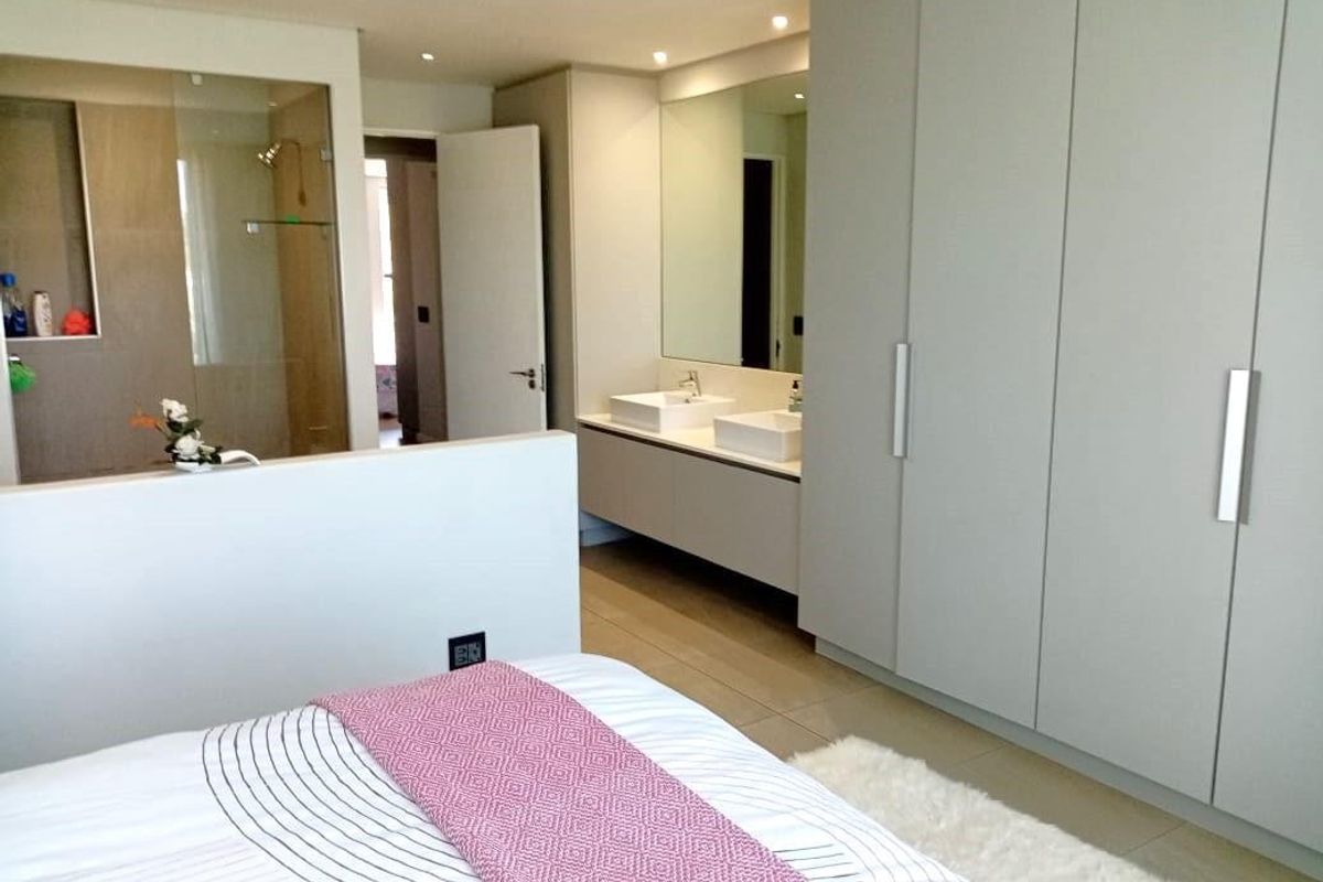 Modern bedroom featuring an open-plan en-suite bathroom with a double vanity, glass shower, and extensive built-in wardrobe storage.