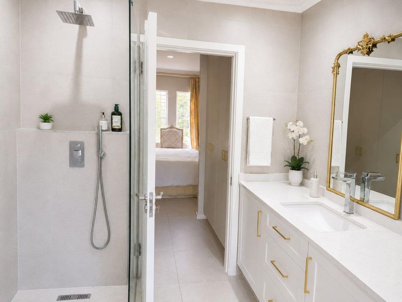 Modern bathroom featuring a walk-in shower with rain head, stone-topped vanity with undermount sink, and neutral tiling, leading into an adjacent bedroom.