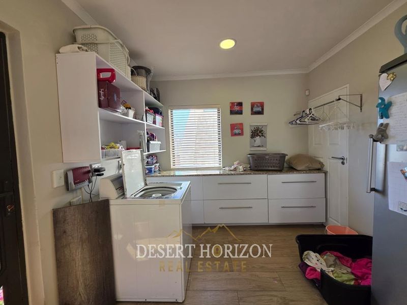 Functional laundry room featuring built-in white cabinetry, granite countertops, wall-mounted shelving, and durable laminate flooring.