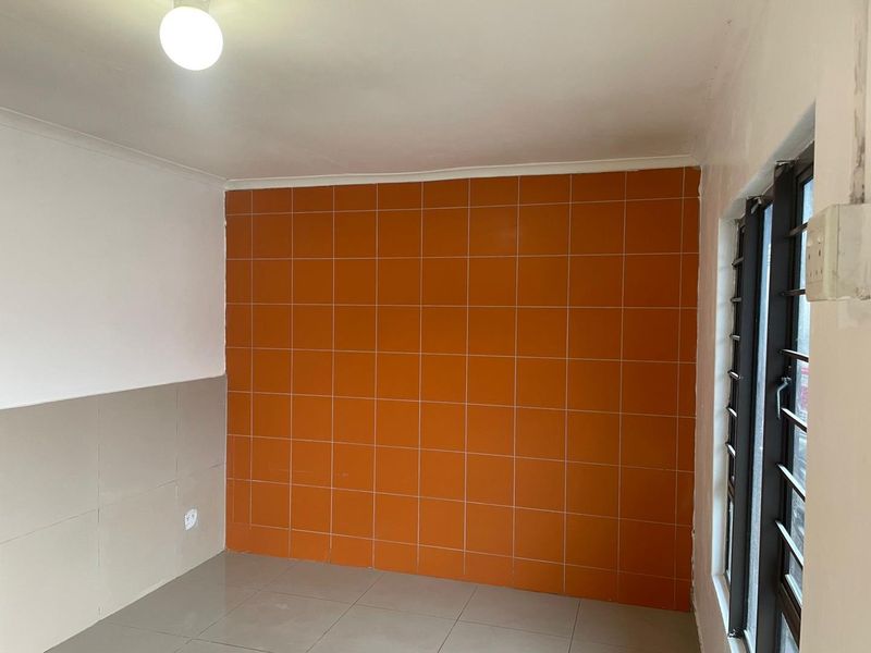 An empty kitchen area featuring dated orange wall tiles, neutral floor tiles, and a louvered window, offering a blank canvas for renovation.