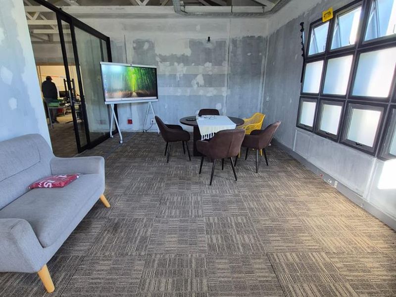Open-plan office space featuring exposed steel roof trusses, carpet tile flooring, and industrial-style grid windows, currently undergoing interior finishing.