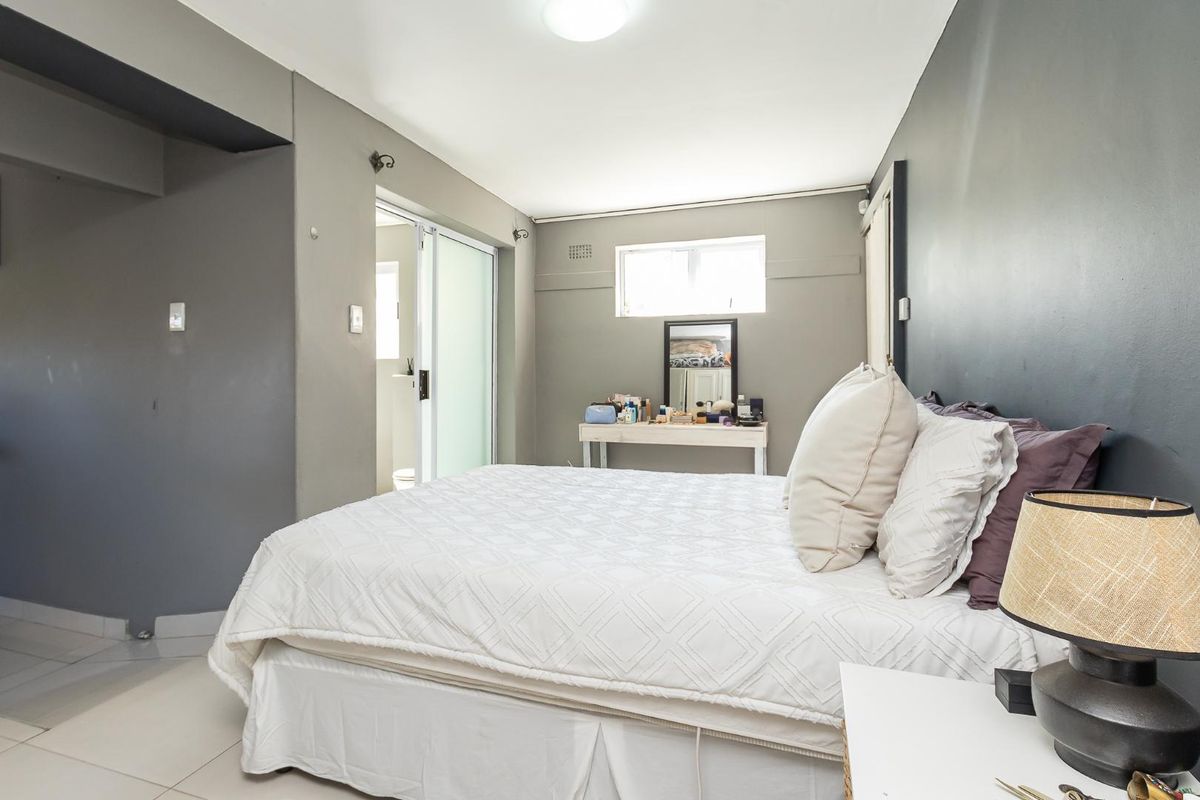 A bedroom featuring neutral grey walls, tiled flooring, and an en-suite bathroom access point with a sliding door.