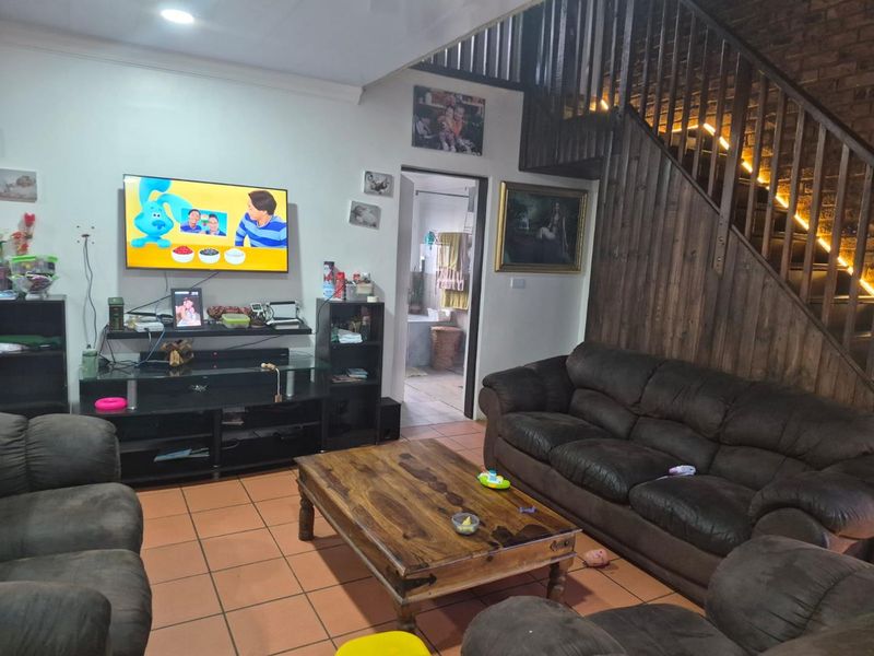 A living room featuring terracotta floor tiles, an exposed brick wall, and a timber staircase leading to the upper level.