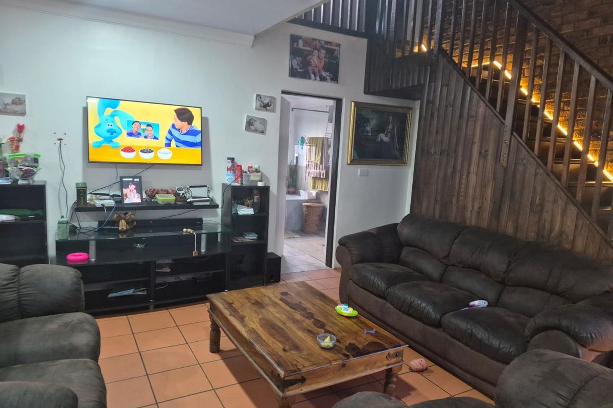 A living room featuring terracotta floor tiles, an exposed brick wall, and a timber staircase leading to the upper level.