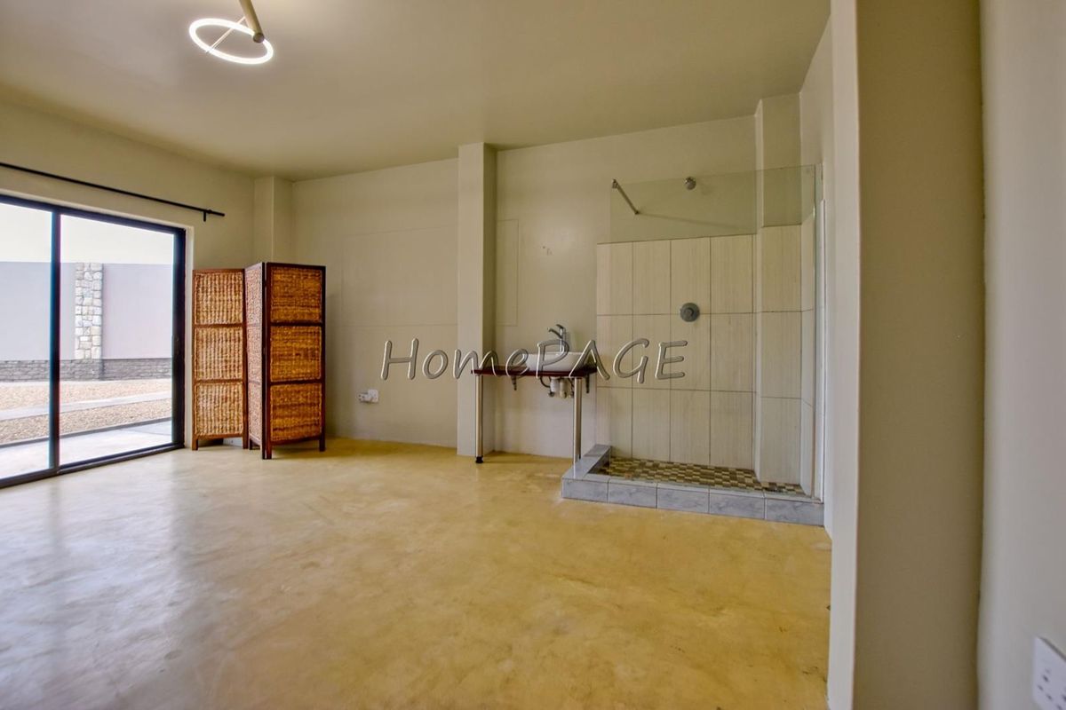 Open-plan bedroom area featuring a walk-in shower, wall-mounted basin, and sliding glass door access to the exterior.