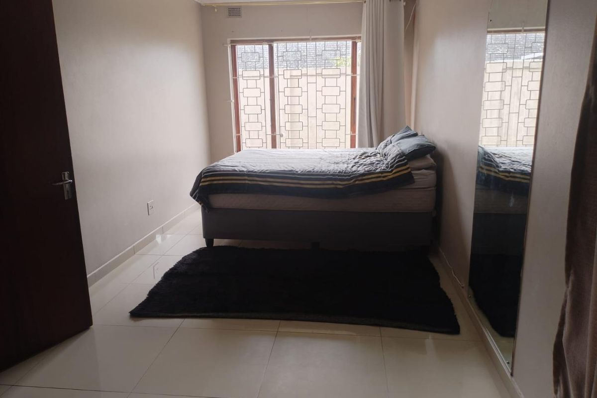 A bedroom featuring tiled flooring, a built-in mirrored wardrobe, and a window fitted with security bars.
