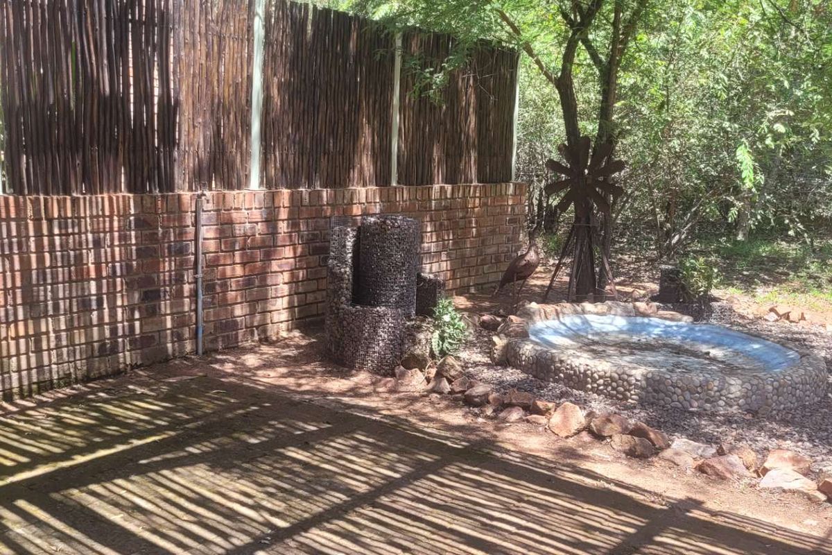 A rear garden area featuring a brick retaining wall, reed privacy screening, a stone-clad water feature, and a small stone-edged pond.