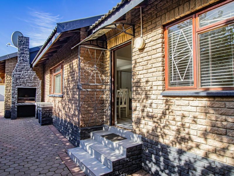 Rear exterior view featuring a brick facade, paved patio area, and a built-in outdoor braai fireplace with direct access to the home.