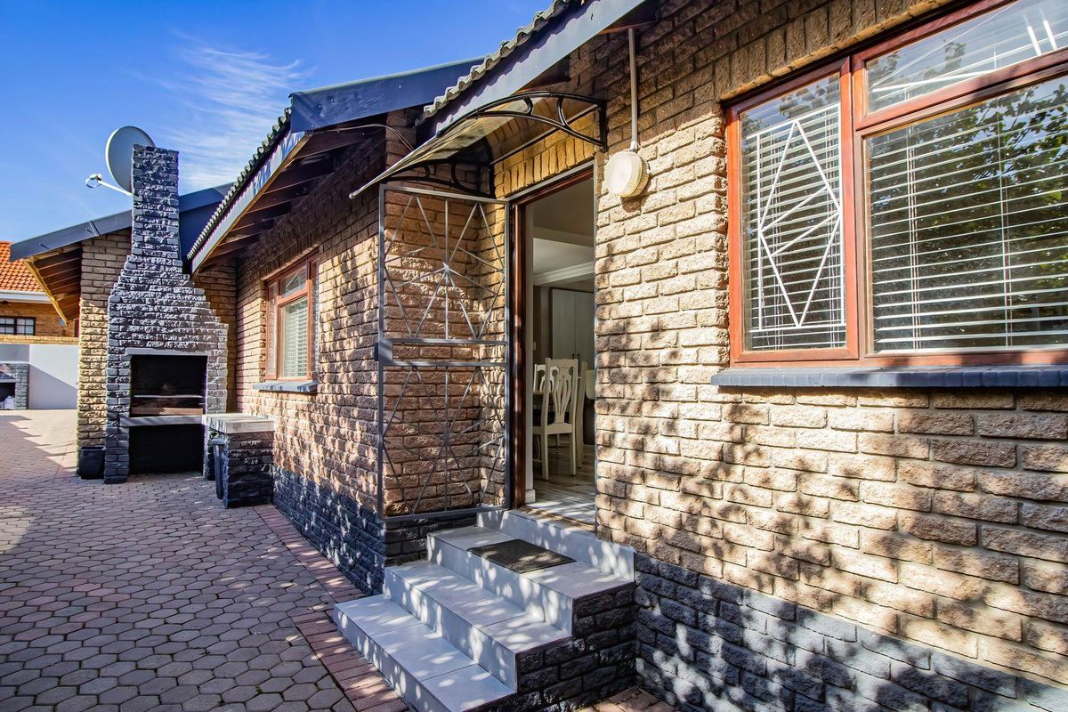 Rear exterior view featuring a brick facade, paved patio area, and a built-in outdoor braai fireplace with direct access to the home.