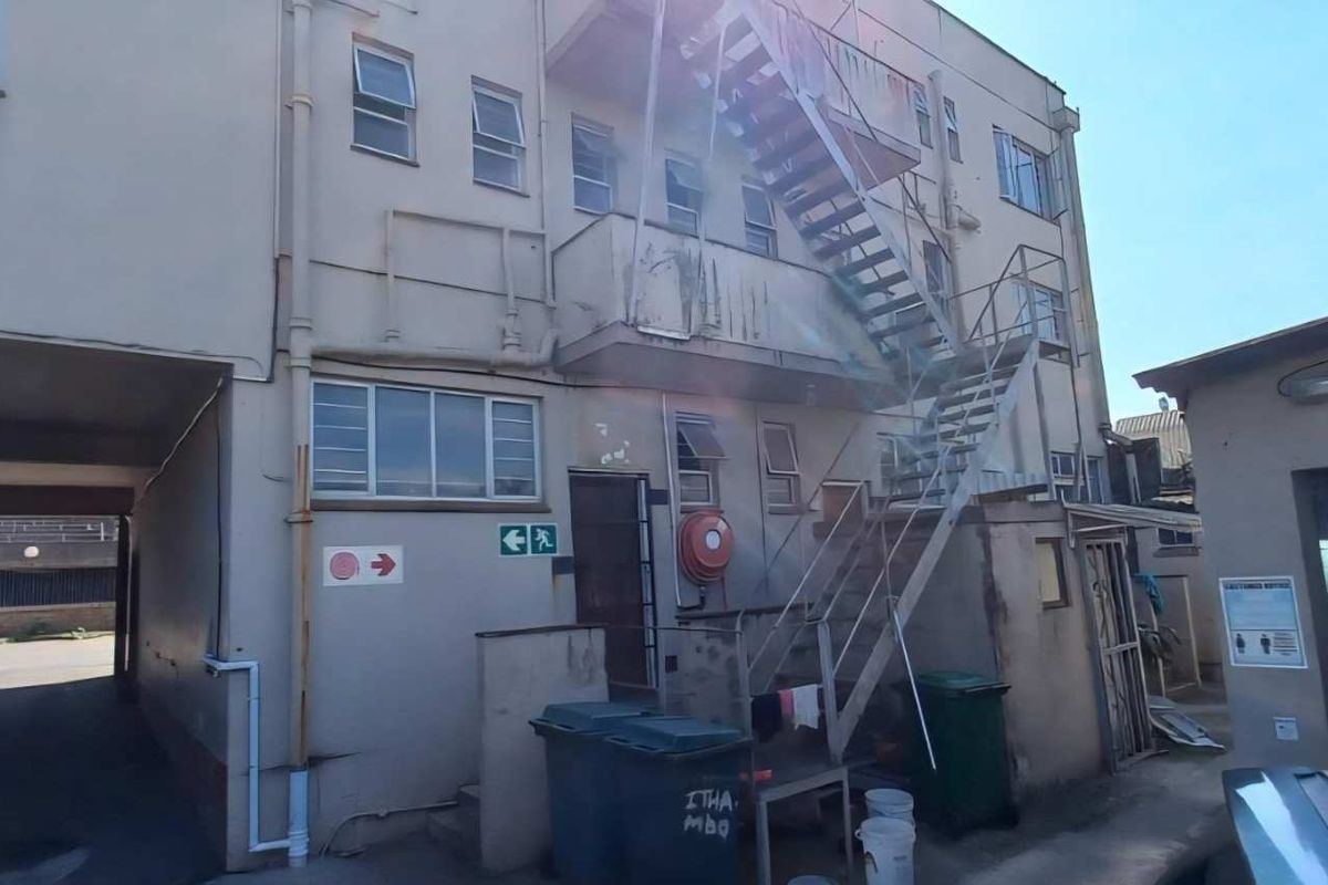 Rear exterior view of an industrial building featuring a metal fire escape staircase, concrete facade, and access to a covered driveway area.