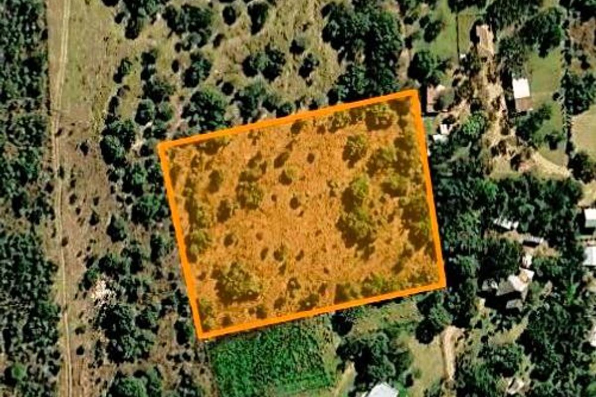 An aerial view of a vacant agricultural plot featuring natural vegetation and open land, highlighted with an orange boundary overlay.