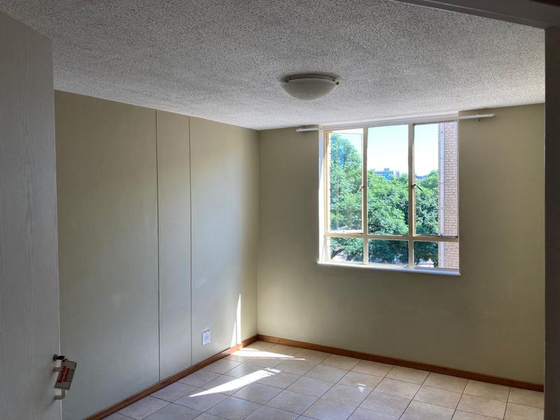 An empty bedroom featuring tiled flooring, a textured ceiling, and a large window providing natural light and an exterior view.