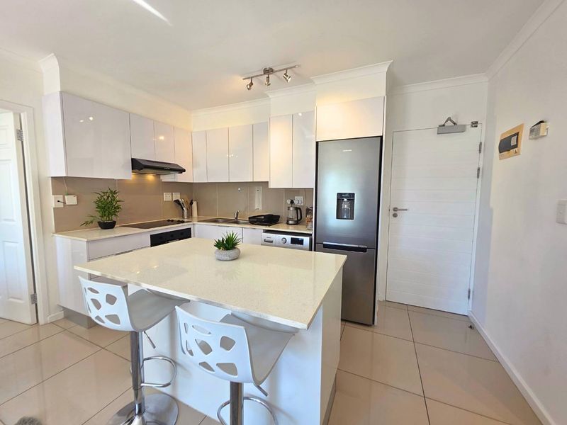 Modern kitchen featuring white gloss cabinetry, stone countertops, a central island, and integrated appliances with neutral tiled flooring.