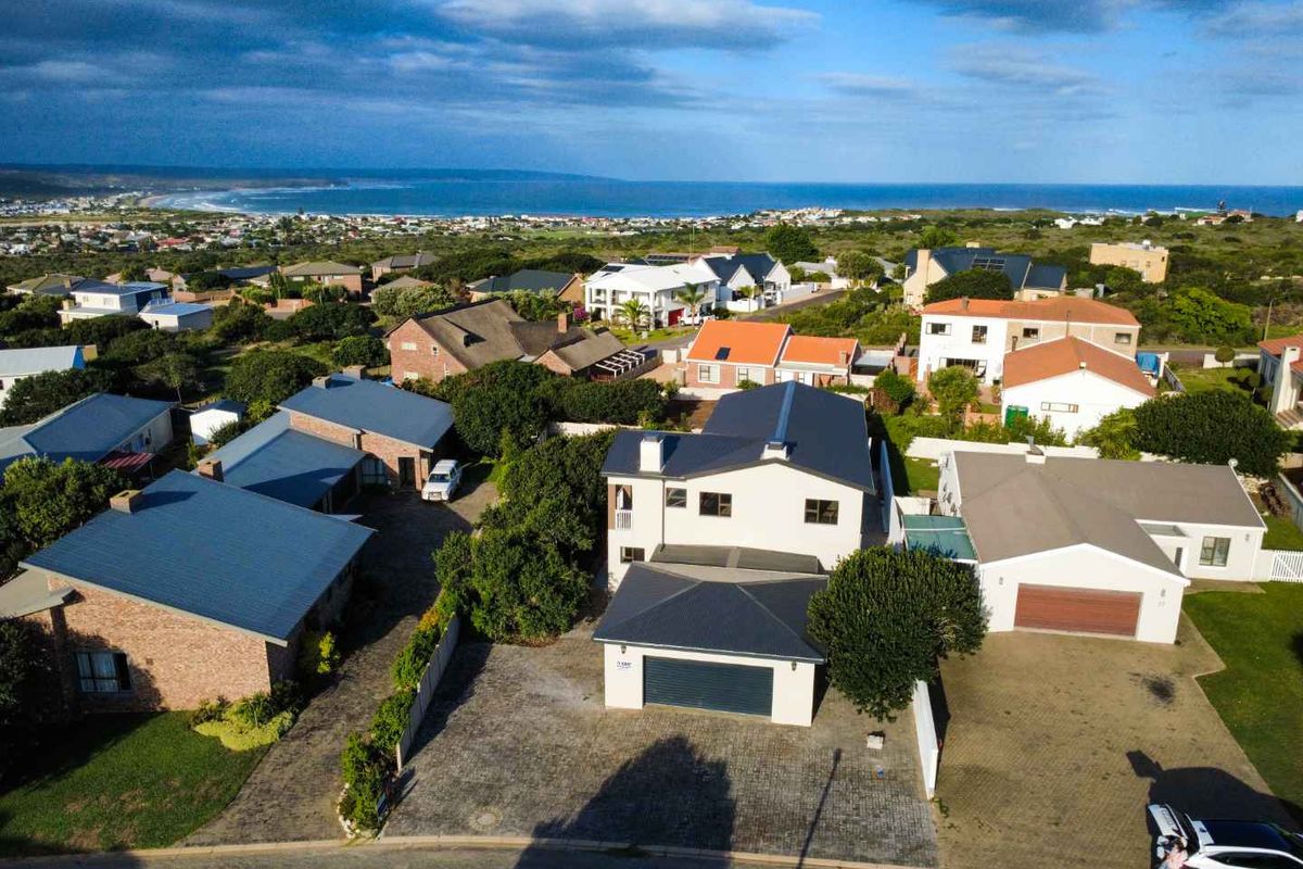 Aerial view of the property showcasing the residential layout, paved driveway, double garage, and surrounding coastal neighbourhood with ocean views.