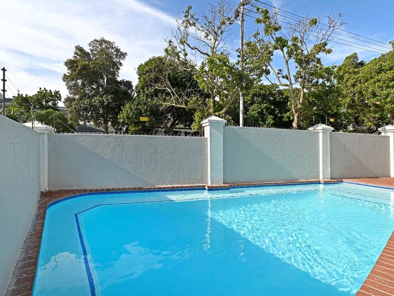 A private swimming pool area featuring a clear pool with brick coping and a secure perimeter wall with electric fencing.