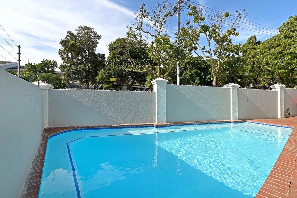 A private swimming pool area featuring a clear pool with brick coping and a secure perimeter wall with electric fencing.