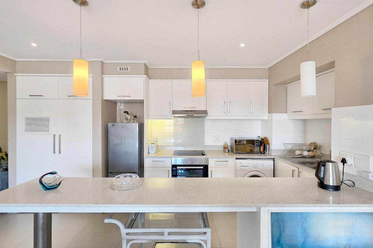 Modern kitchen featuring white cabinetry, stone countertops, built-in oven and hob, extractor fan, and integrated washing machine with a breakfast bar.