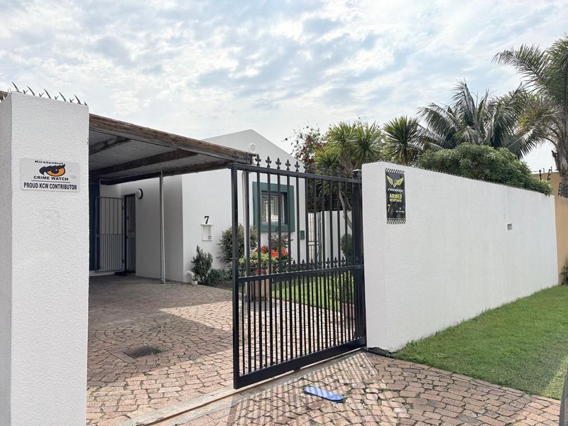 Front exterior view featuring a paved driveway, covered carport, and secure perimeter wall with metal gate and security features.
