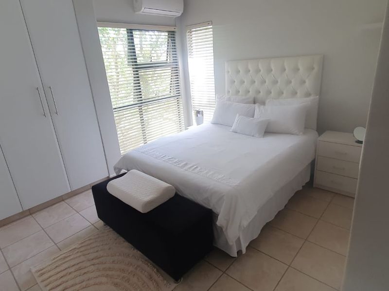 A well-maintained bedroom featuring built-in cupboards, tiled flooring, and a wall-mounted air conditioning unit with natural light through venetian blinds.
