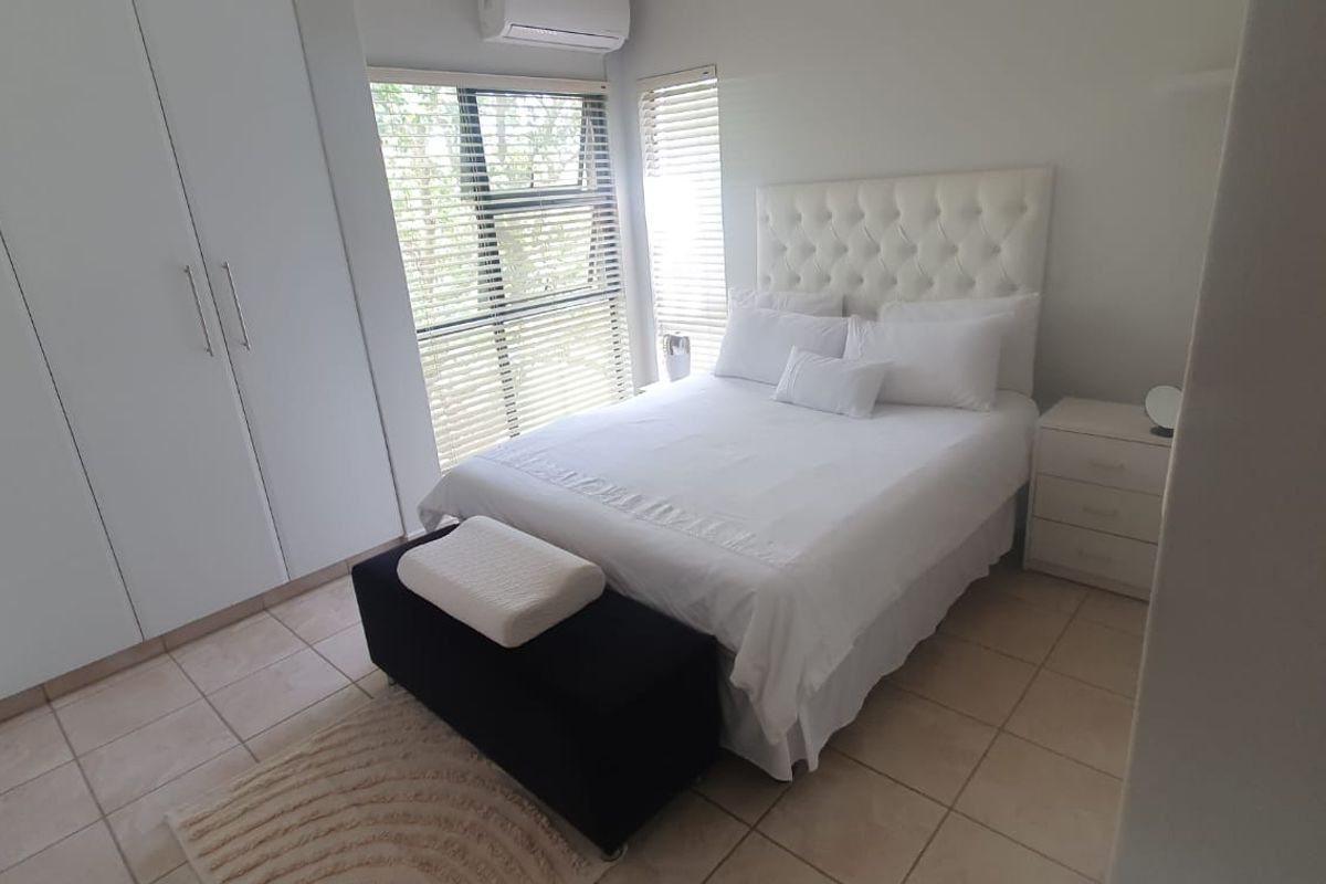 A well-maintained bedroom featuring built-in cupboards, tiled flooring, and a wall-mounted air conditioning unit with natural light through venetian blinds.