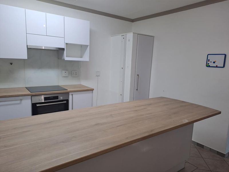 Modern kitchen featuring white cabinetry, wood-look laminate countertops, a central island, and integrated appliances including an oven and hob.