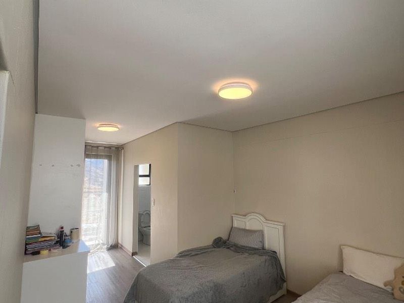 A functional bedroom featuring laminate flooring, dual ceiling lights, and direct access to an en-suite bathroom through a sliding glass door.