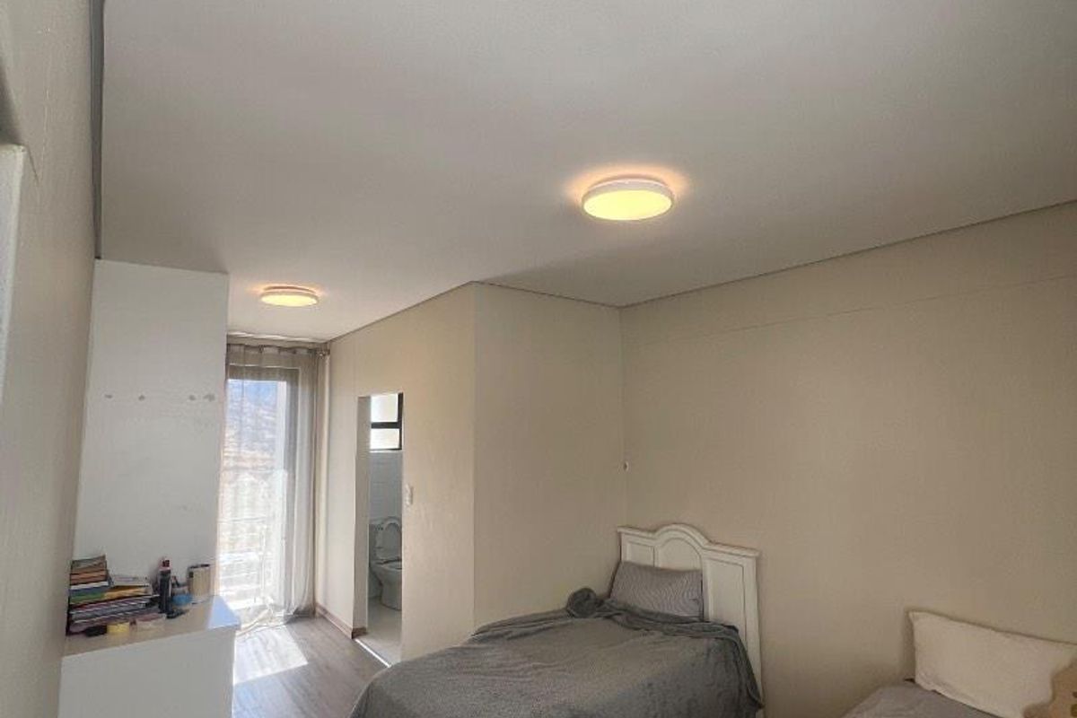 A functional bedroom featuring laminate flooring, dual ceiling lights, and direct access to an en-suite bathroom through a sliding glass door.