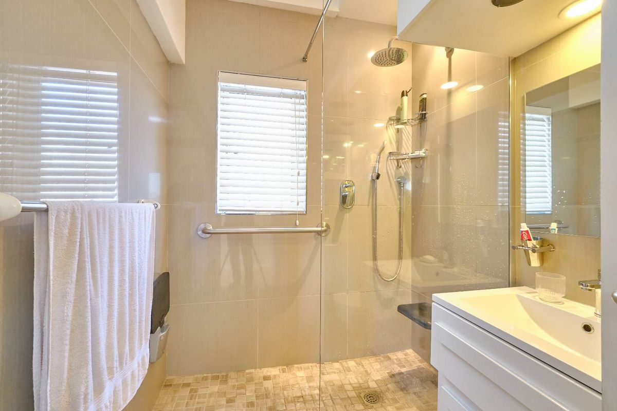 Modern bathroom featuring a spacious walk-in shower with glass screen, rain shower head, grab rail, and a sleek vanity basin.
