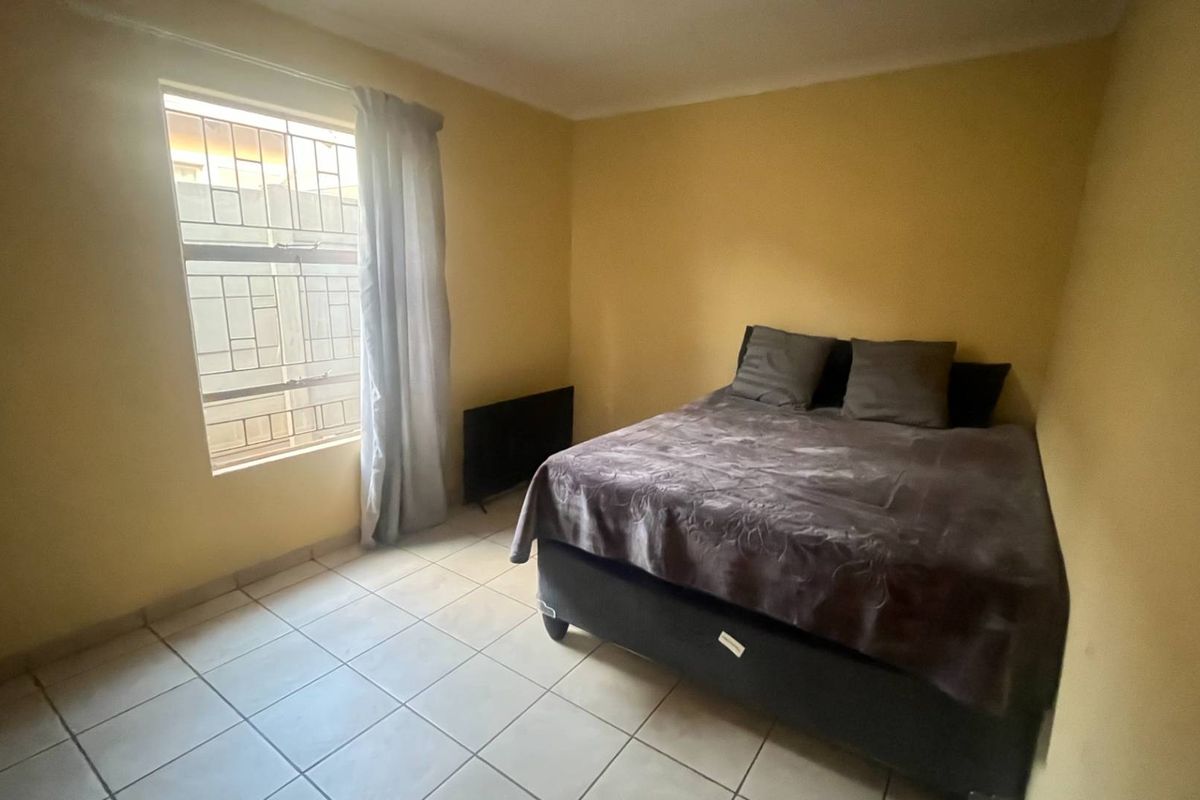A bedroom featuring tiled flooring and a window fitted with security bars, requiring cosmetic updates to the wall finishes.