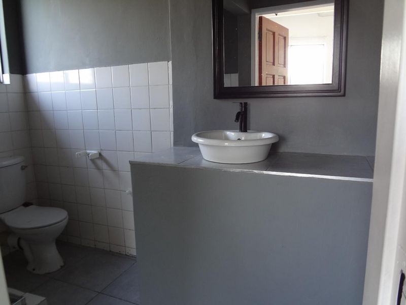 A functional bathroom featuring a vessel sink, wall-mounted mirror, and toilet with tiled splashback finishes.