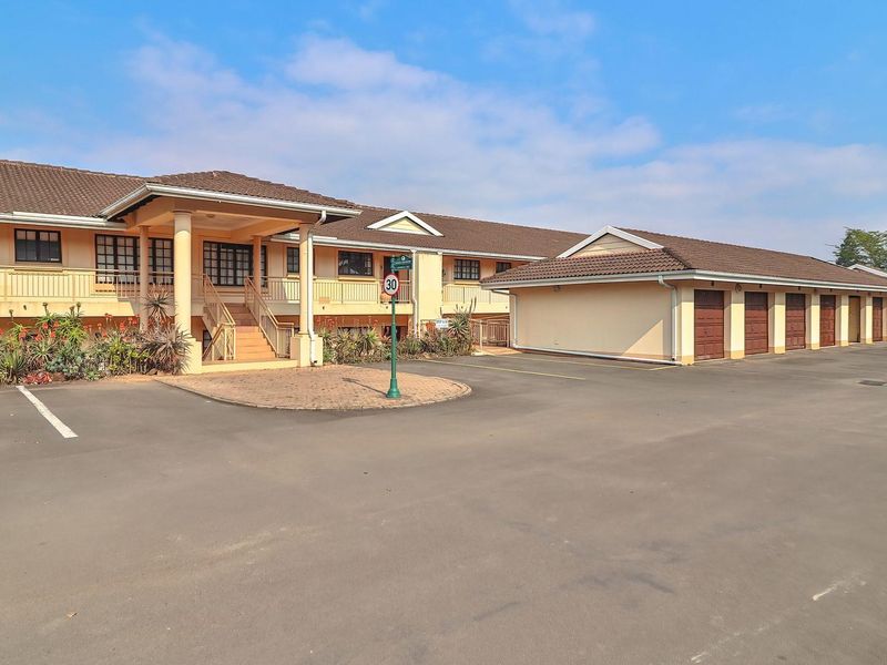 Front exterior view of the apartment complex featuring a paved driveway, covered entrance, and a row of garage units.