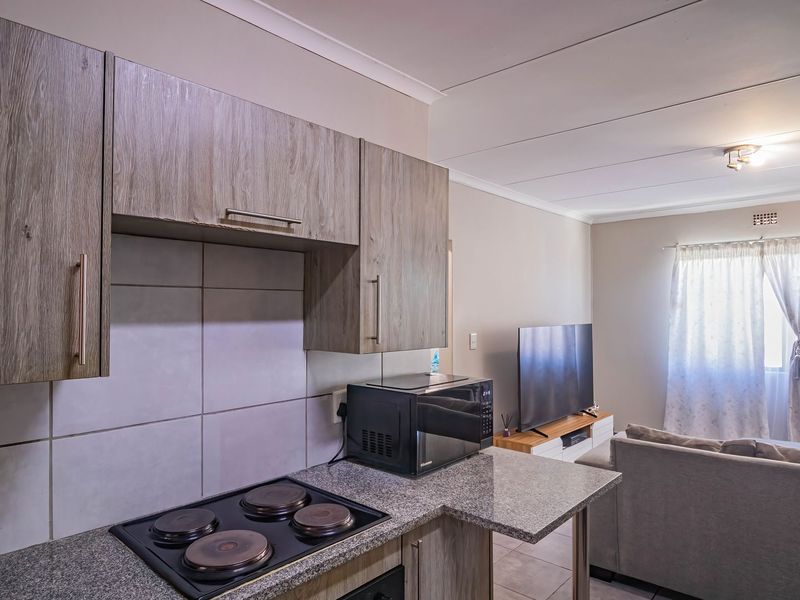 Open plan living area featuring a modern kitchen with laminate cabinetry, granite countertops, and an integrated electric hob, flowing into the adjacent lounge space.