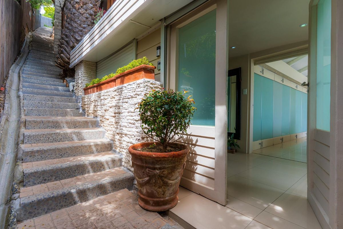 Rear exterior view featuring a stone retaining wall, concrete staircase, and access to the interior through a sliding glass door.