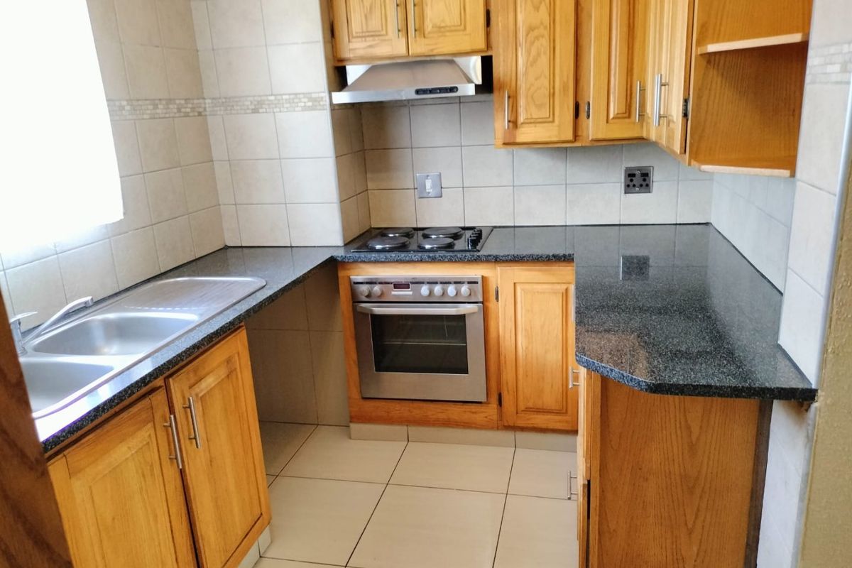 A functional kitchen featuring wooden cabinetry, granite countertops, a double stainless steel sink, and built-in oven with an electric hob.