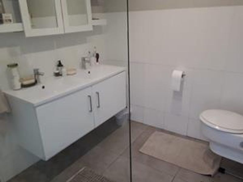 Modern bathroom featuring a wall-mounted double vanity with dual basins, a wall-hung toilet, and a glass shower screen with neutral tiled finishes.