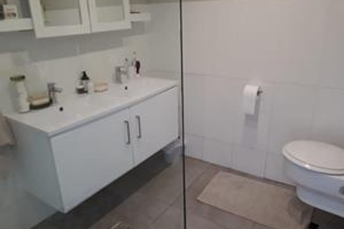 Modern bathroom featuring a wall-mounted double vanity with dual basins, a wall-hung toilet, and a glass shower screen with neutral tiled finishes.