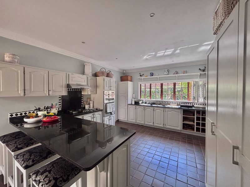 Spacious kitchen featuring granite countertops, built-in oven, gas hob, extractor fan, and ample cabinetry with a classic tiled floor finish.