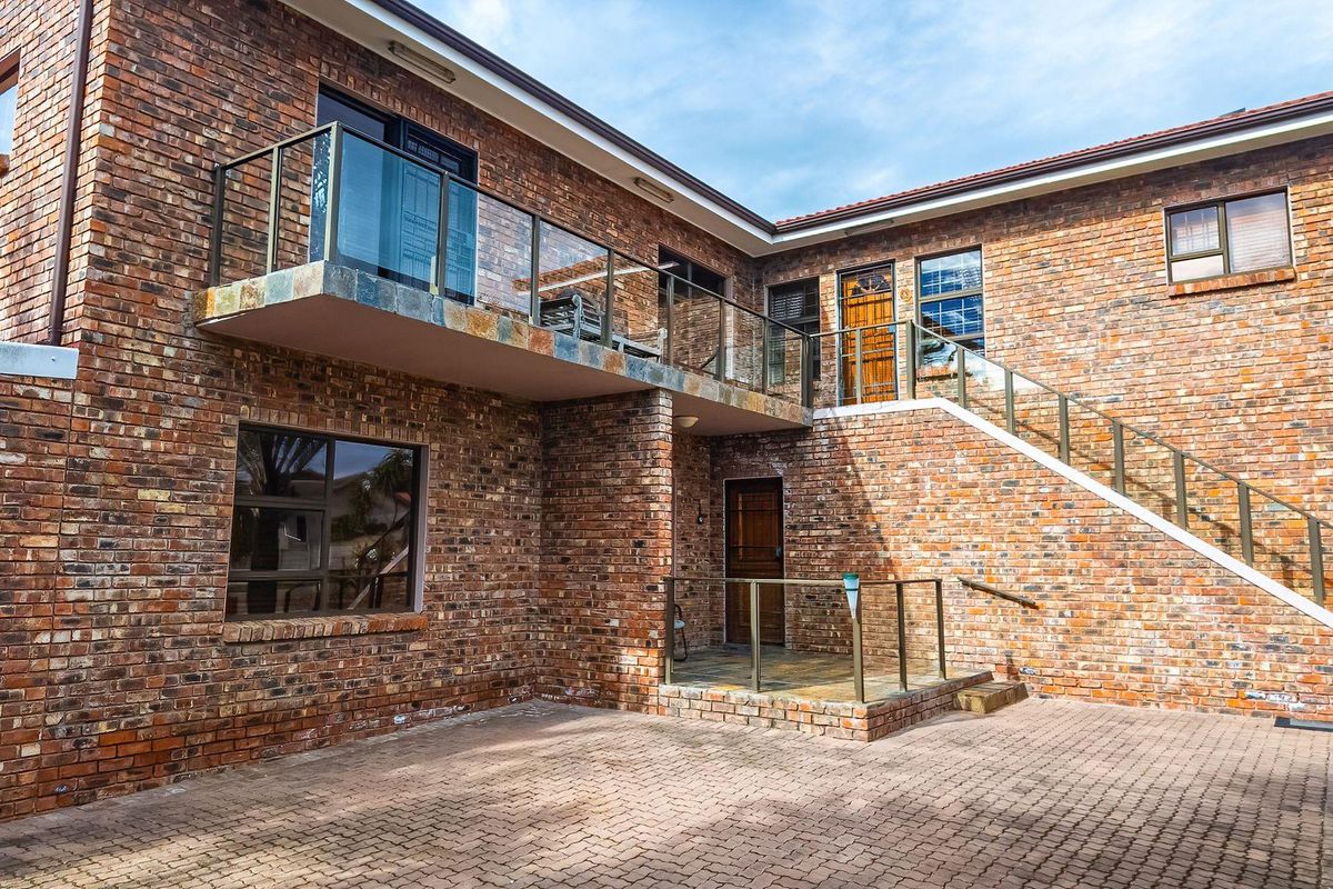 A well-maintained double-storey face brick residence featuring a paved courtyard, external staircase, and glass-railed upper balcony.