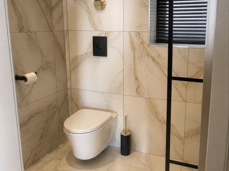 Modern bathroom featuring high-end marble-effect tiling, a sleek wall-mounted toilet with a concealed cistern, and a window with fitted blinds.