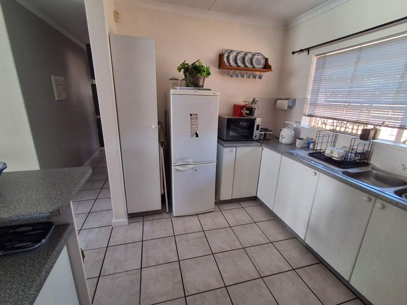 A functional kitchen featuring laminate cabinetry, durable countertops, a stainless steel double sink, and ceramic floor tiles, offering a practical layout for daily use.