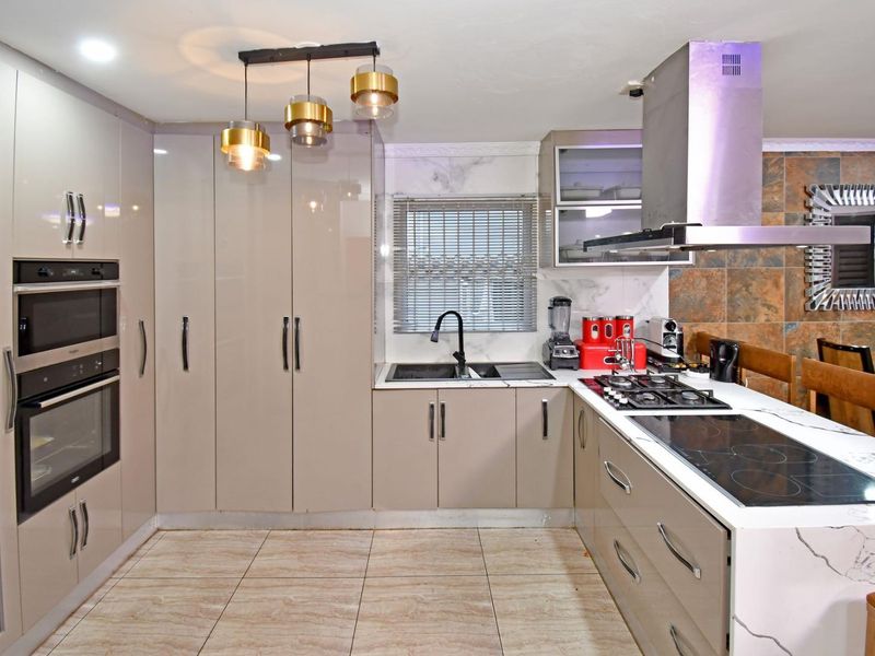 Modern kitchen featuring high-gloss cabinetry, stone countertops, dual hobs, built-in oven and microwave, and contemporary pendant lighting.