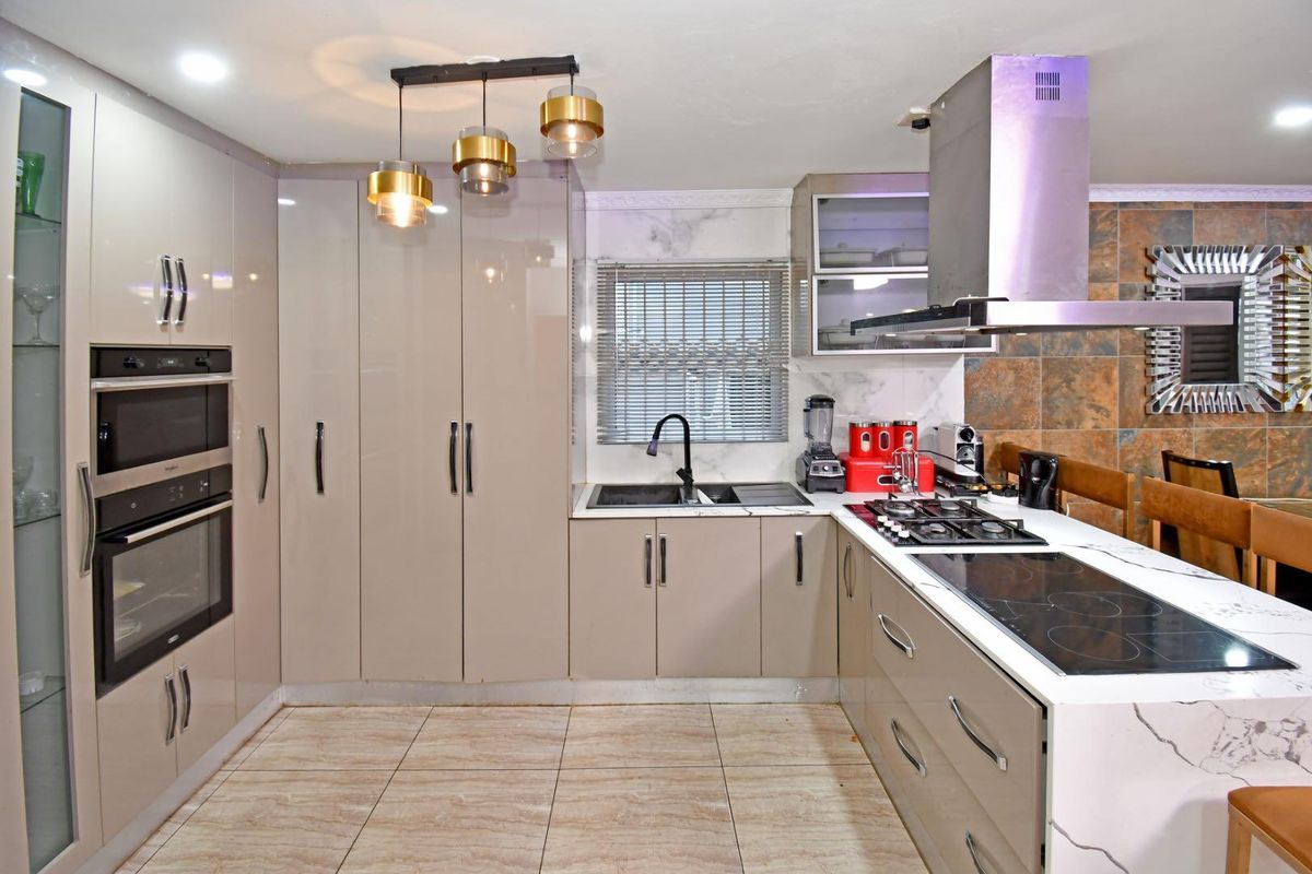 Modern kitchen featuring high-gloss cabinetry, stone countertops, dual hobs, built-in oven and microwave, and contemporary pendant lighting.