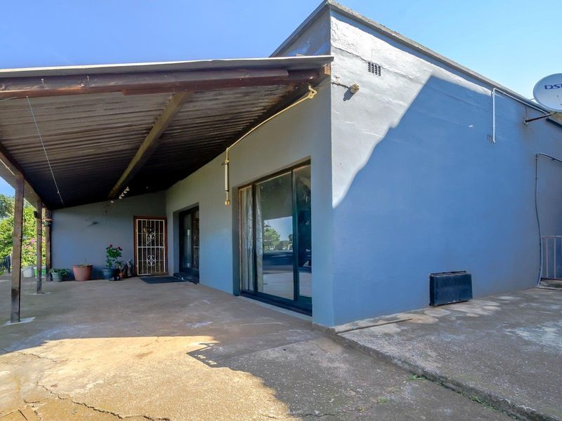 Rear exterior view featuring a covered patio area with concrete flooring, sliding glass doors, and a security gate entrance.