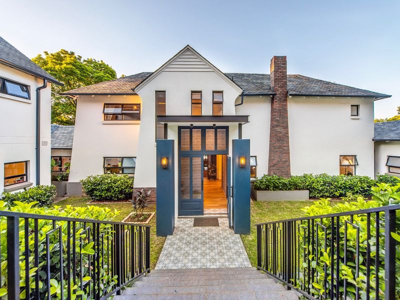 A beautifully maintained front facade featuring a striking brick chimney, modern entrance portico, and a patterned tiled walkway leading to the main door.