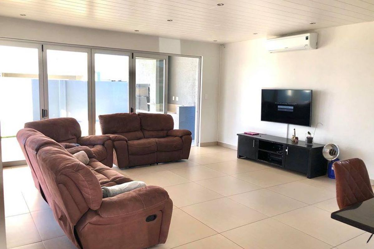 Spacious living room featuring large sliding glass doors leading to an outdoor area, tiled flooring, recessed ceiling lighting, and a wall-mounted air conditioning unit.